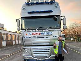 Man in high-visibility vest holding paperwork in front of a DAF truck with "GS DRIVER TRAINING" branding, symbolizing HGV training and career opportunities in the transport industry.